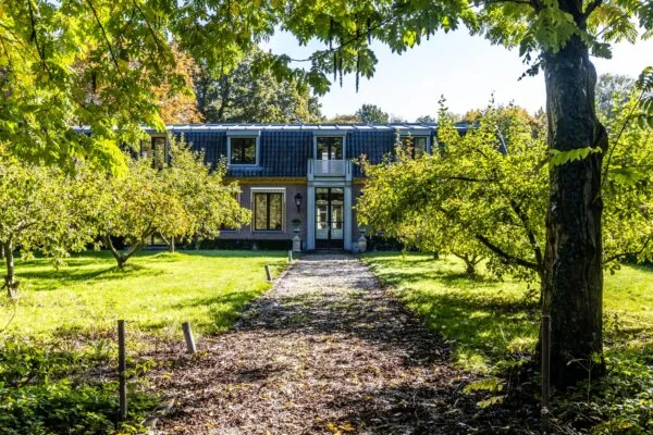 Pad door een groene tuin leidt naar een brede woning aan de Langbroekerdijk in zonnig herfstlicht.